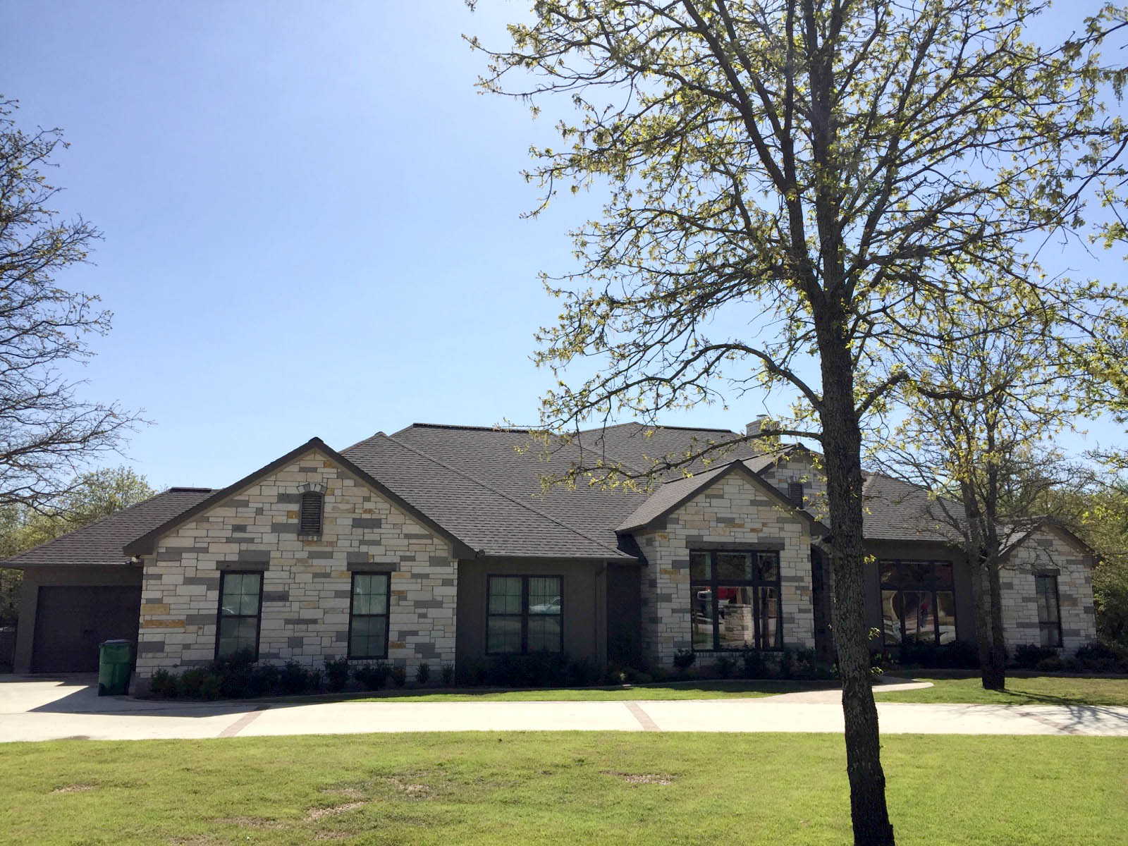 Completed roof on modern stone home with charcoal shingles and stone exterior — Heritage Roofing TX