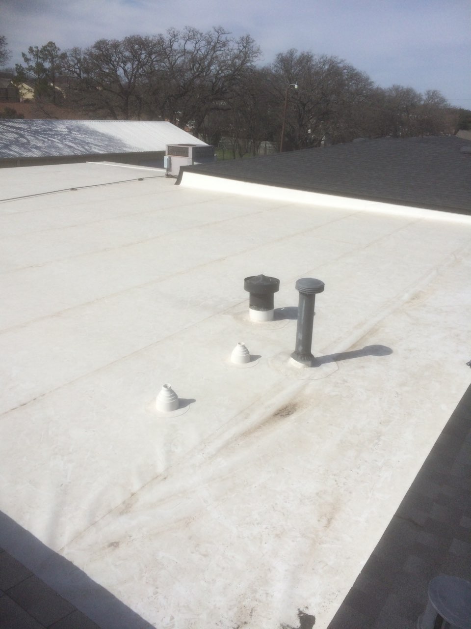 White TPO flat roof with pipe boots and HVAC penetrations on commercial building — Heritage Roofing TX